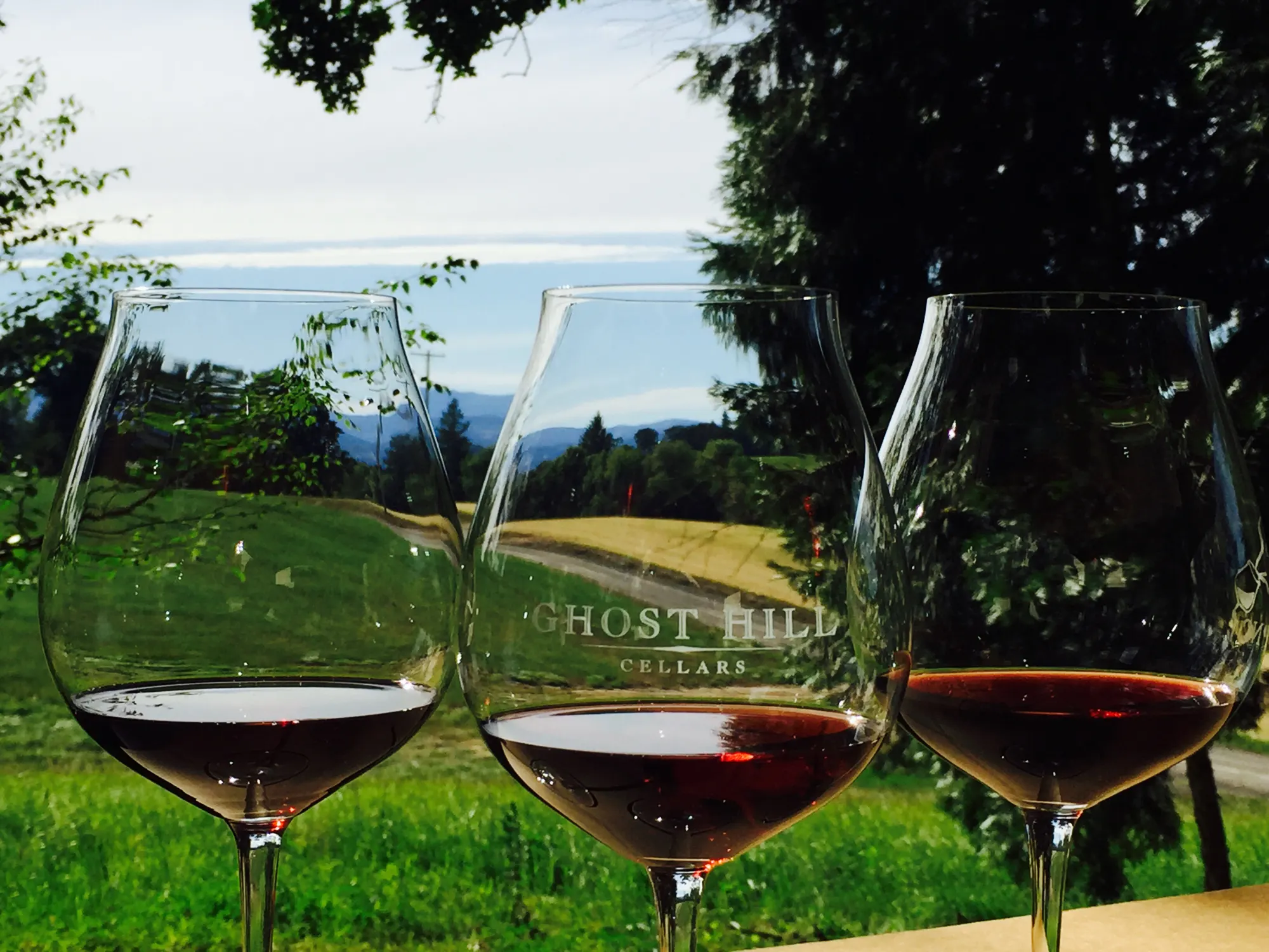 Three glasses of Ghost Hill Cellars Pinot Noir with a beautiful view beyond